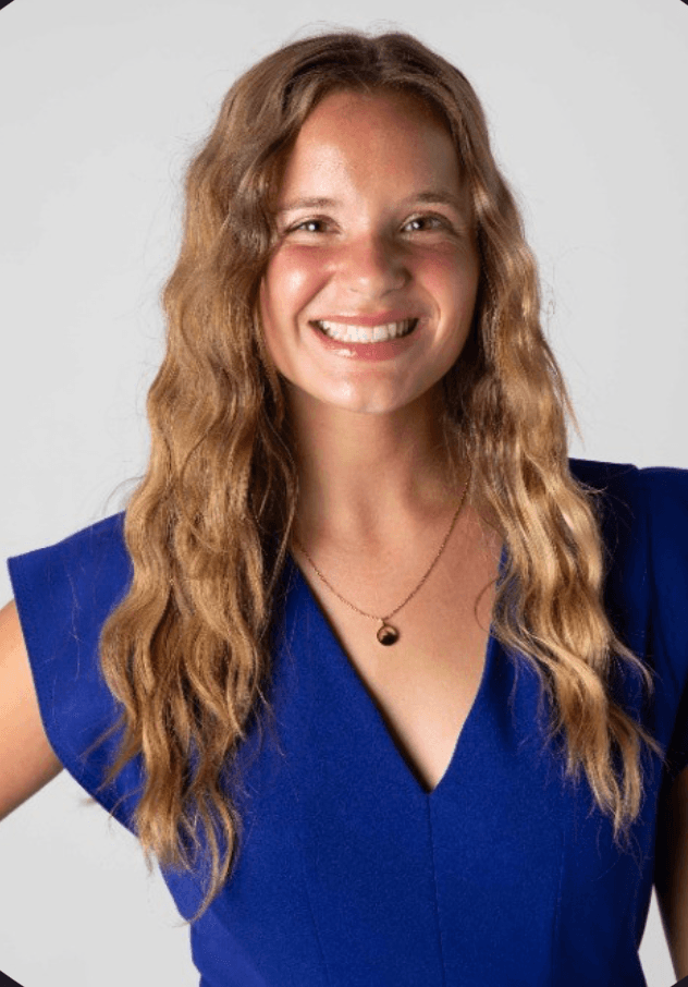 Josephine, a young woman with long wavy fair hair in a blue dress, smiling against a plain studio background
